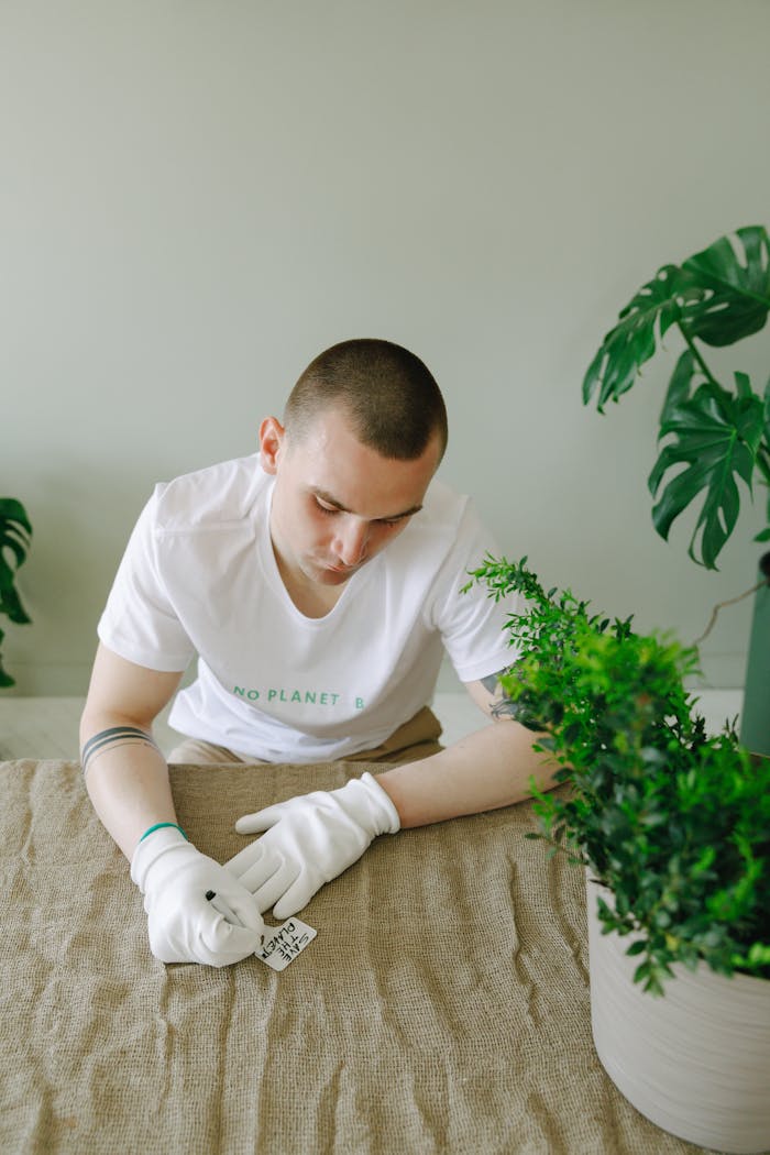 A man wearing gloves caring for indoor plants on a table, promoting eco-friendly lifestyle.
