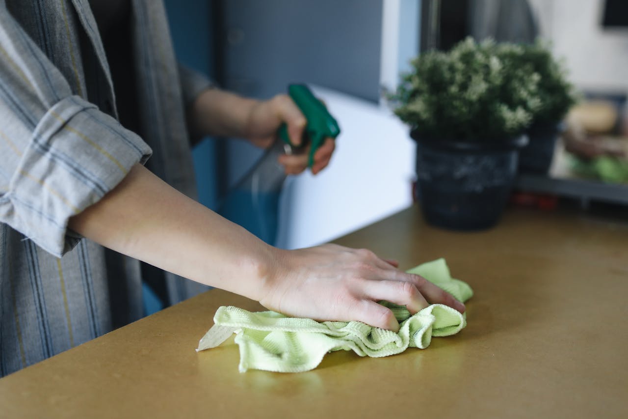 hero-img Close-up of a woman wiping a table with a spray bottle and cloth indoors, symbolizing effective housekeeping.